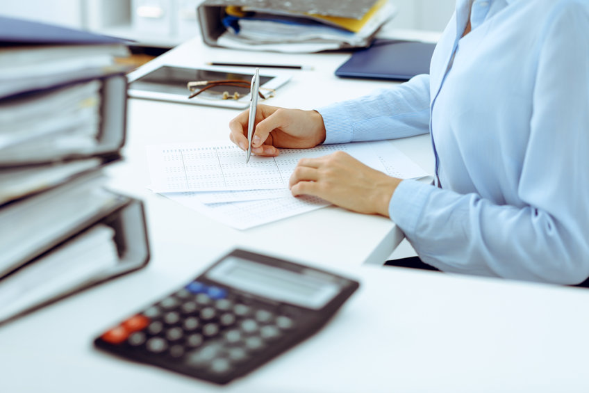 Calculator and binders with papers are waiting to be processed by business woman or bookkeeper back in blur. Internal Audit and tax concept